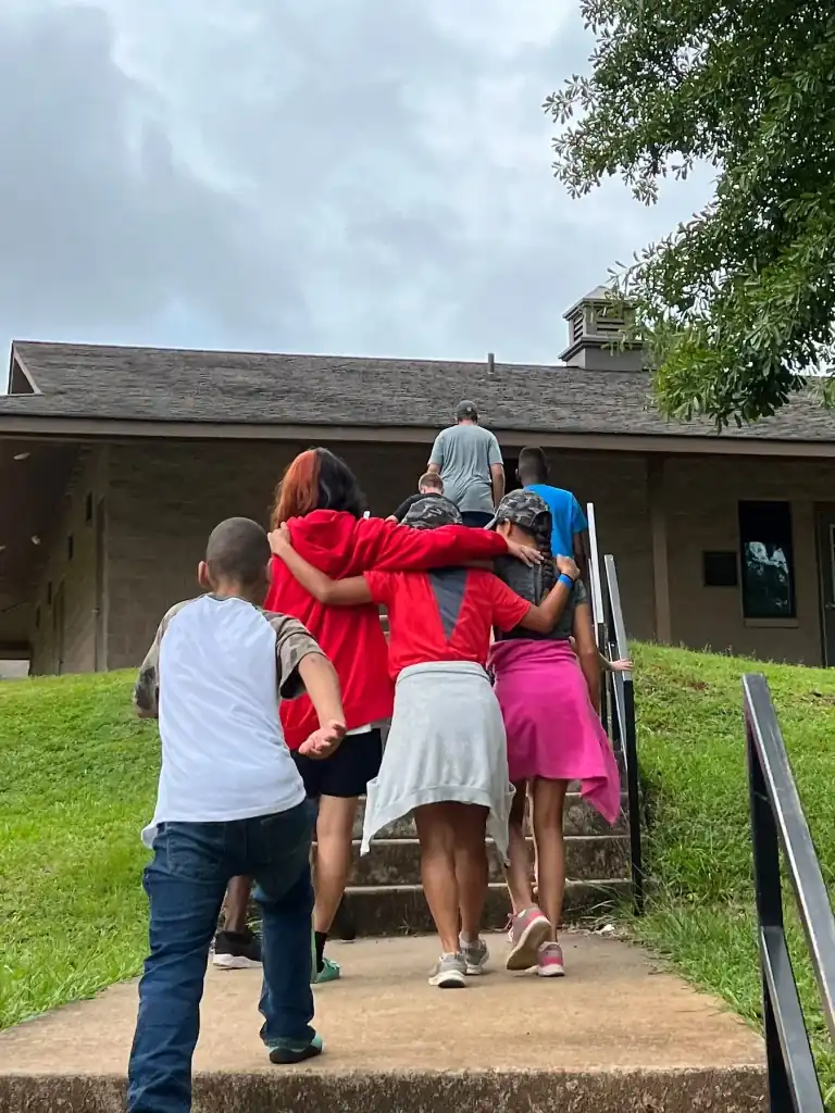 A group of campers ascend a staircase leading to a building.  They're walking close together, some with arms around each other.