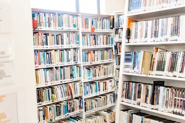 White bookshelves filled with various books and media in a library setting.