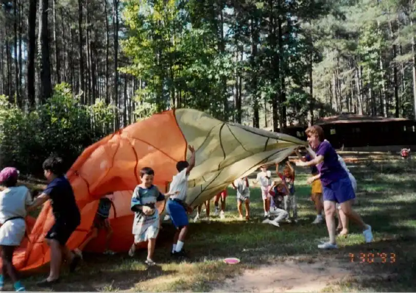 Campers and staff playing with a parachute in a wooded area at Camp Juliena