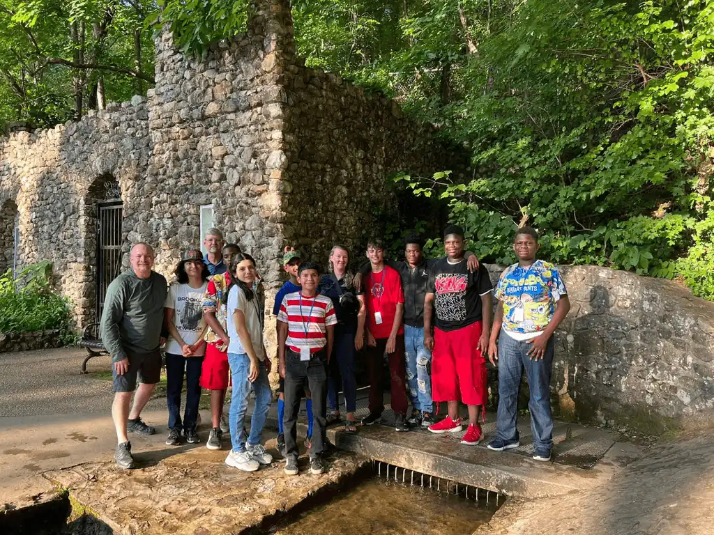 High school students stand together for a group photo outside an old stone structure. Trees are in the background.