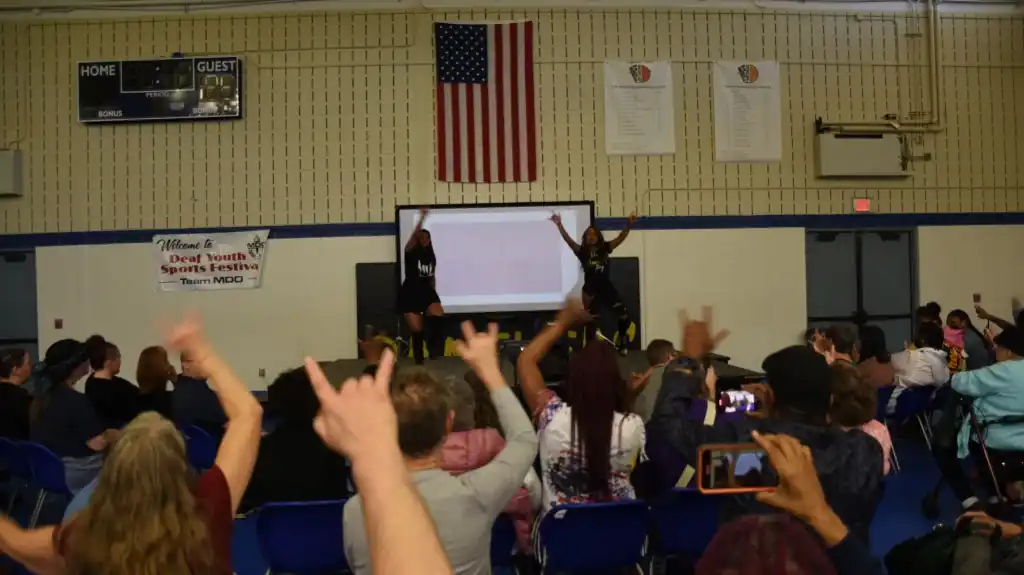 Two performers on stage at DEAFestival while the audience cheers and raises the ILY sign
