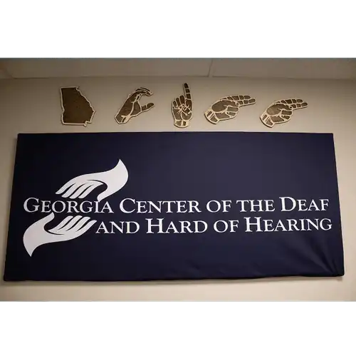 GCDHH wall decoration, blue sign with GCDHH logo, wood hangings in the shape of the state of GA, and hands spelling out GCDHH.