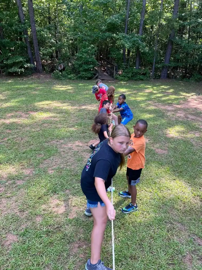 Campers playing tug-of-war outdoors on a grassy field.