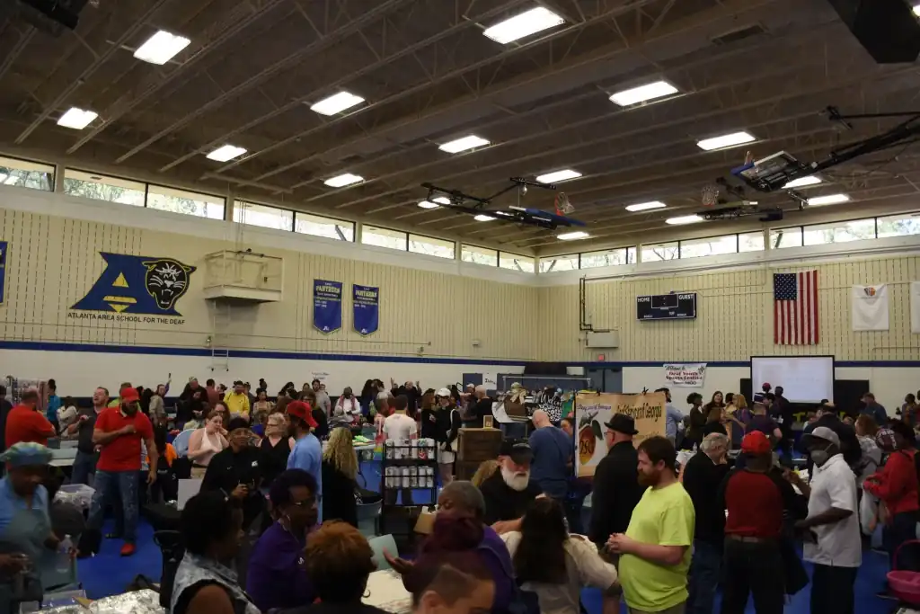 A large indoor venue filled with people browsing tables at a craft fair or market.