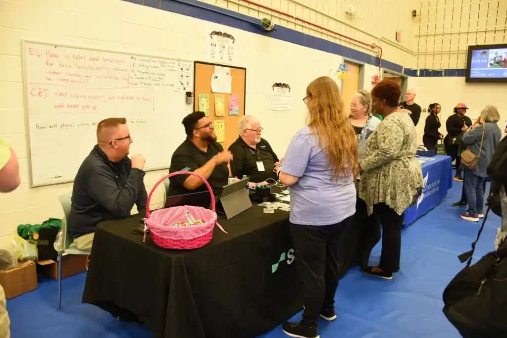 People at a table at a community event.  A pink basket sits on the table.