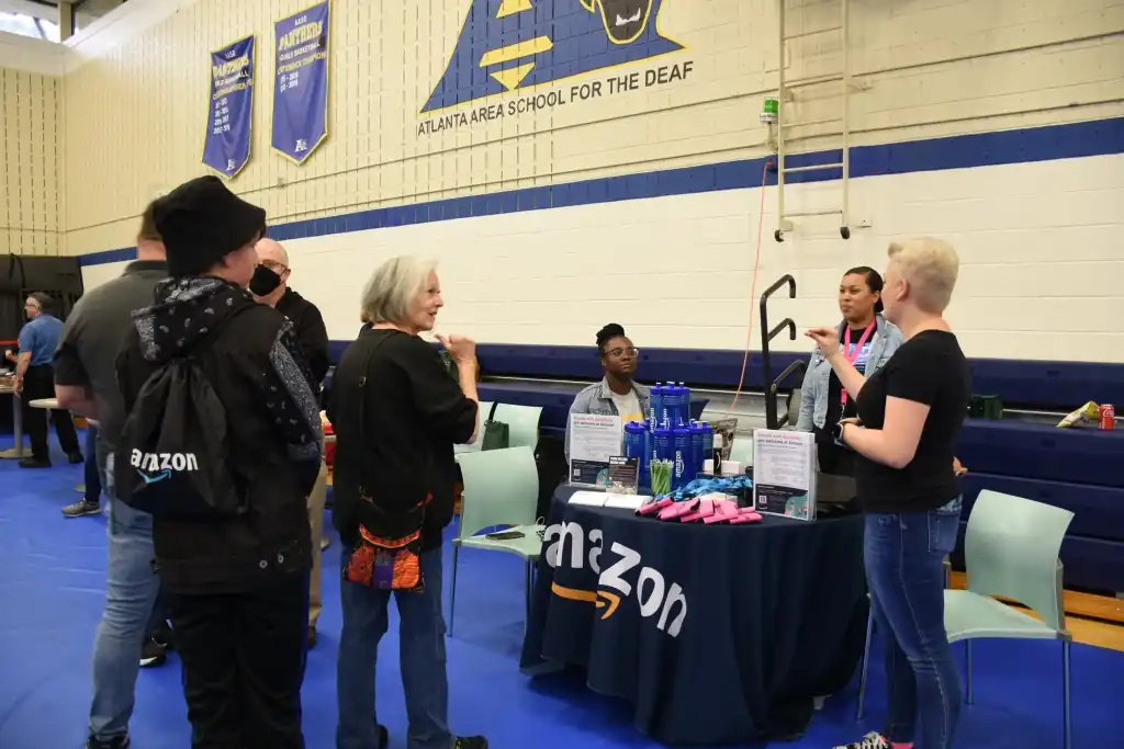 Amazon representatives talk with students at a career fair.  A table displays Amazon branding and products.